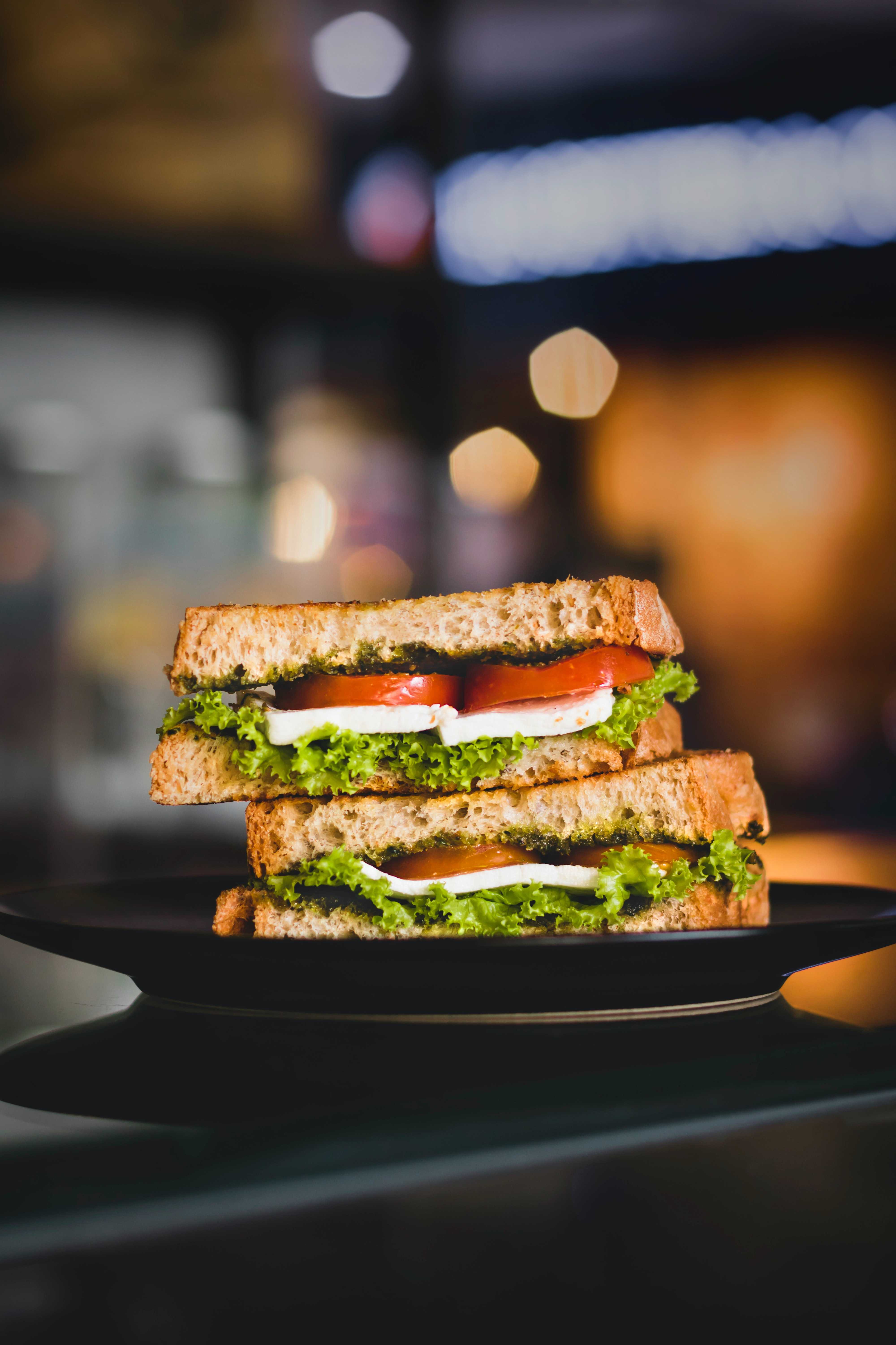 Two sandwiches stacked on a black plate with a blurred background